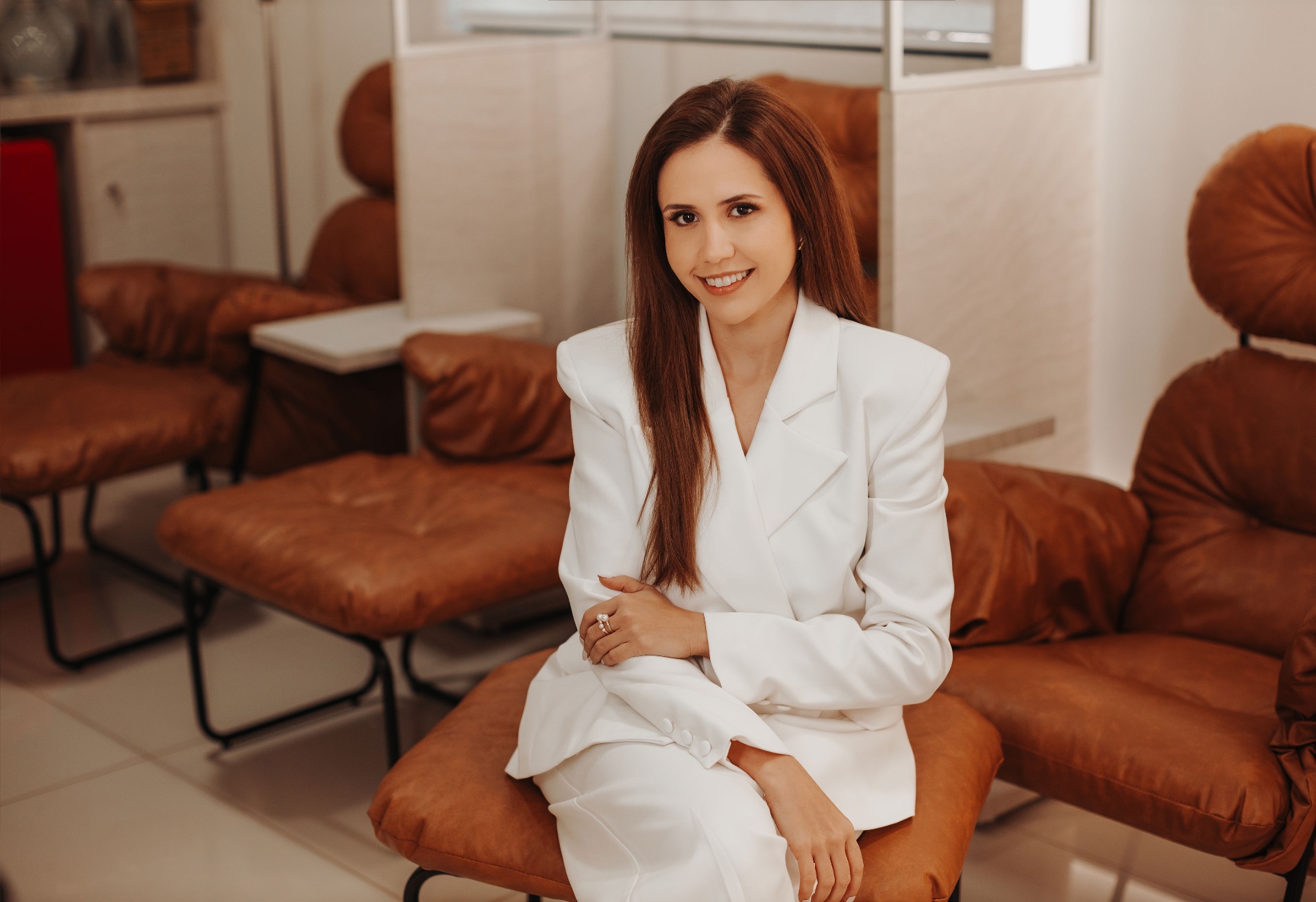Dra. Daniella Andretta sentada em poltrona de couro marrom no ambiente de acolhimento